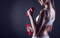 Fitness girl with dumbbells on a dark background. Back view